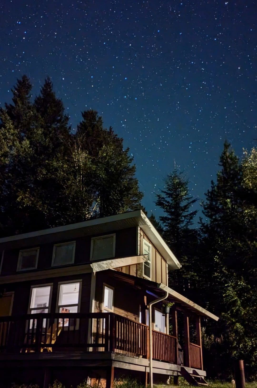 The cabin is nestled among tall trees under a clear starry sky. Soft light emanates from the windows, illuminating the structure's exterior and inviting a sense of quiet tranquility.