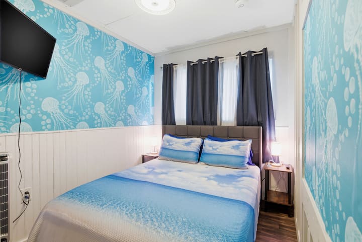 Siesta Key 度假屋内这间舒适的卧室配有一张标准双人床，采用海洋主题装饰，包括章鱼图案的床上用品和一幅色彩鲜艳的水母壁画，营造出轻松惬意的海滨氛围。