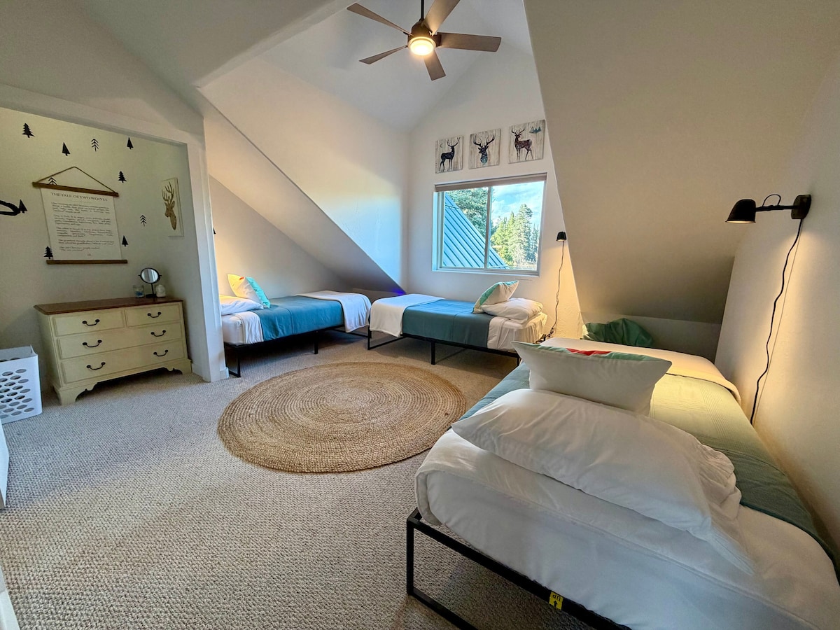 Sur le côté droit, cette chambre offre trois lits jumeaux, également équipés de literie haut de gamme, et comprend un charmant coin lecture niché sous la pente du toit, avec deux fauteuils poires et un panier rempli de livres pour enfants.