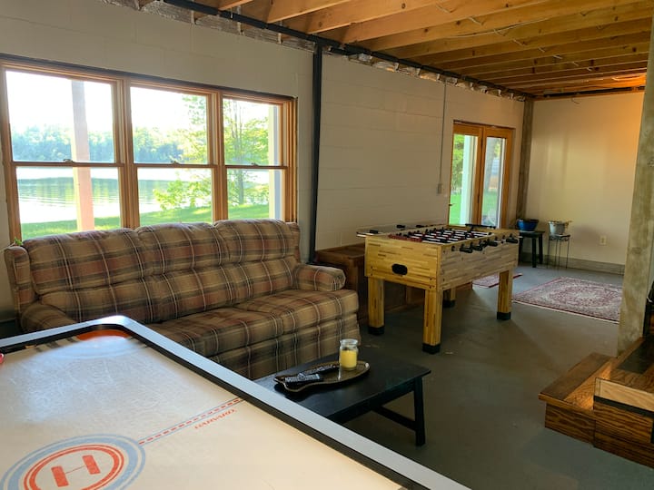 The basement hangout space includes a queen pullout couch, big screen TV, foosball, air hockey, and French doors opening onto the lower deck, all with a beautiful lake view
