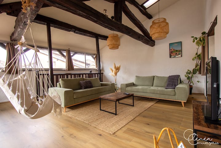 Sebule kubwa yenye mwangaza na mihimili inayoonekana, sofa mbili za starehe, mojawapo ikiwa sofa-kitanda ya 140 x 200, televisheni na kiti cha kukalia kinachoning'inia katika mazingira ya uchangamfu na yenye mvuto.