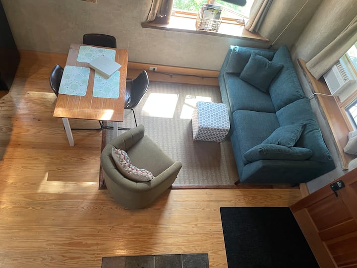 The roomy living room features a comfortable small couch with an ottoman, encircled with windows, an extra blanket and a dining table that seats 3.  The couch can be slept on as a small bed.