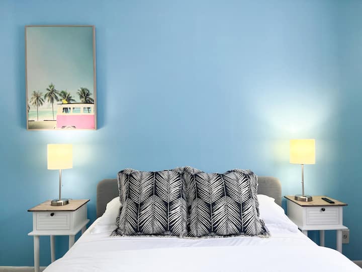 להירגע בחדר השינה התוסס הזה בהשראת החוף, עם קיר מבטא כחול מרשים ועיצוב טרופי. המיטה הנעימה עם כרית מודגשת ממוסגרת על ידי תאורה רכה, ויוצרת אווירה חמה. מושלם להירגע אחרי יום בחוף הים!