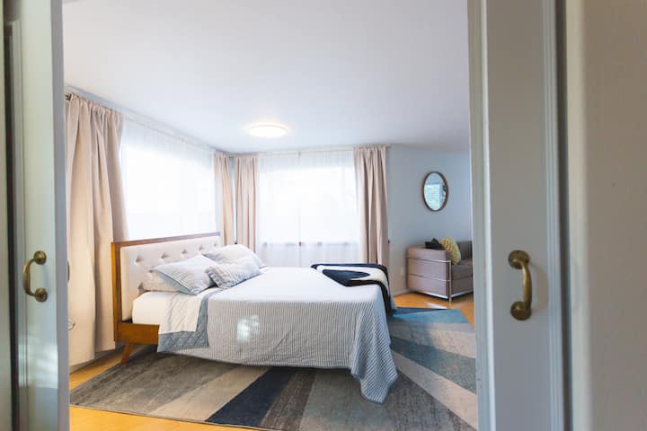 La chambre comprend un lit « queen », un placard de rangement, une table de nuit avec une lampe et un générateur de bruit blanc. La chambre est très spacieuse, les fenêtres laissent entrer la lumière naturelle et offrent une vue.