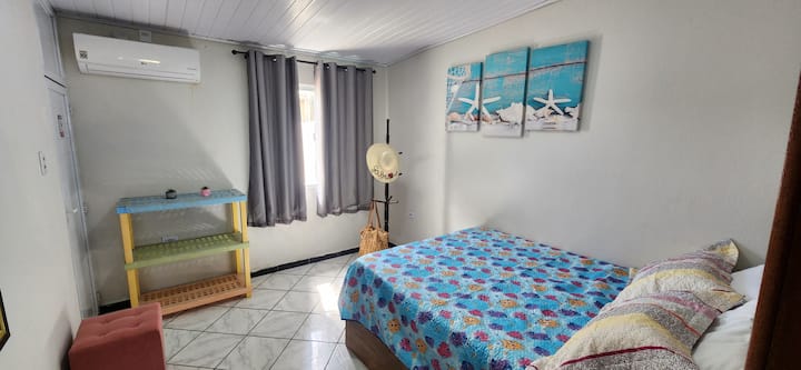 DORMITORIO 1: cama doble muy grande, aire acondicionado, marco de fotos montado en la pared, espejo, perchero, puf y estante para objetos.