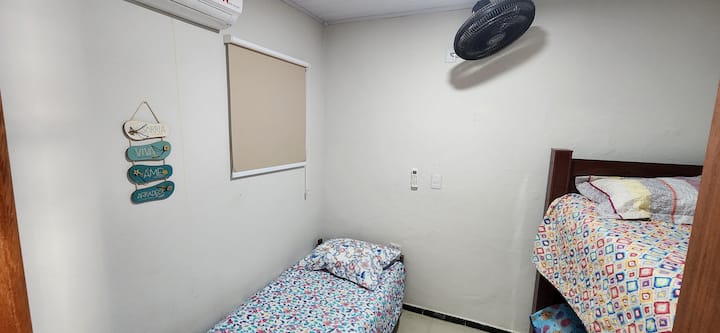 HABITACIÓN 4: esta es la habitación más pequeña de la casa con una cama individual, litera, aire acondicionado, ventilador de pared, espejo, ventilador móvil y estante para objetos.