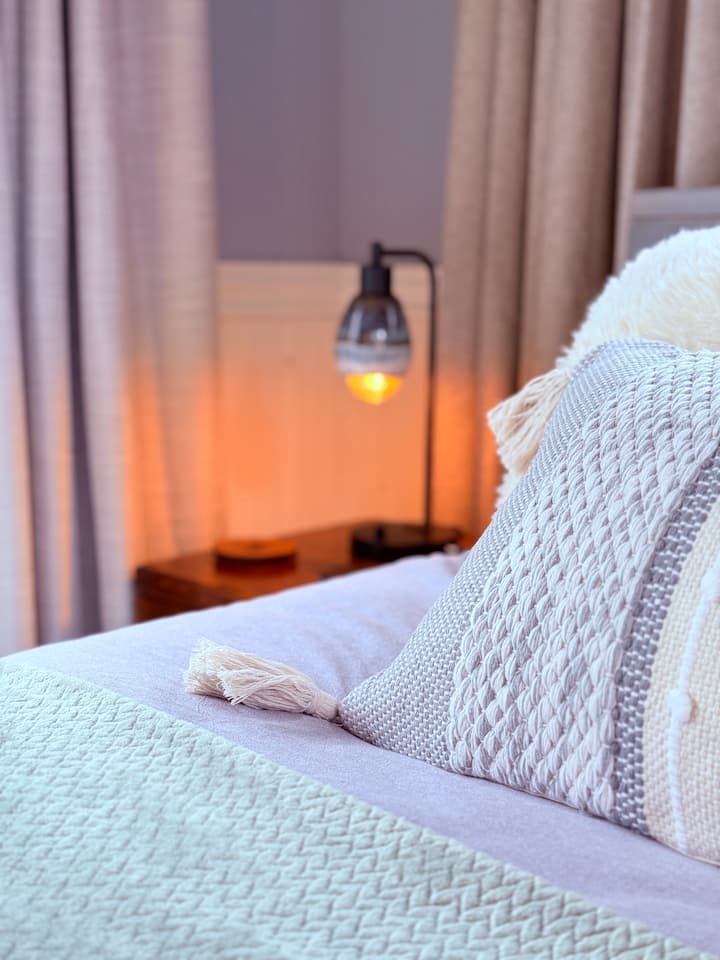 Romantic bedroom with a plush queen bed facing a large projector screen for cozy movie nights. Private balcony overlooks a peaceful river. Soft lighting and warm décor create an intimate feel, with the added convenience of an ensuite half bathroom.