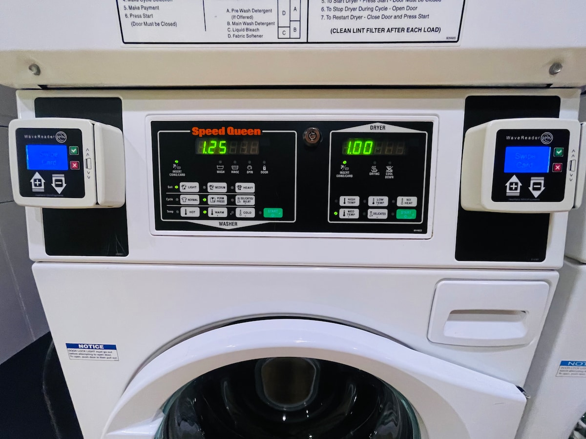 A card-operated washer and dryer unit is displayed, featuring digital control panels with buttons for different settings. The machine showcases a clean and modern design, with clear displays indicating the wash time and cycle selections.