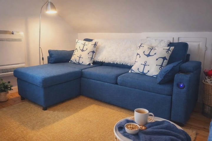 Comodo divano con chaise longue per sedersi con i piedi sollevati. Dispone inoltre di caricabatterie USB integrati. Se necessario, può anche essere trasformato in un letto matrimoniale estraibile