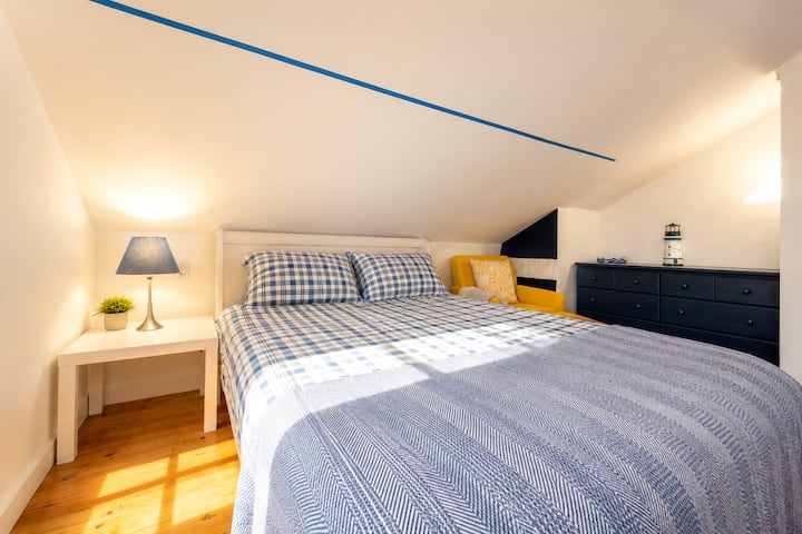 Relax in this bright and inviting coastal-inspired bedroom featuring a comfortable queen bed, soft linens, and charming nautical décor. A cozy reading chair and warm, welcoming atmosphere make it the perfect place to unwind.