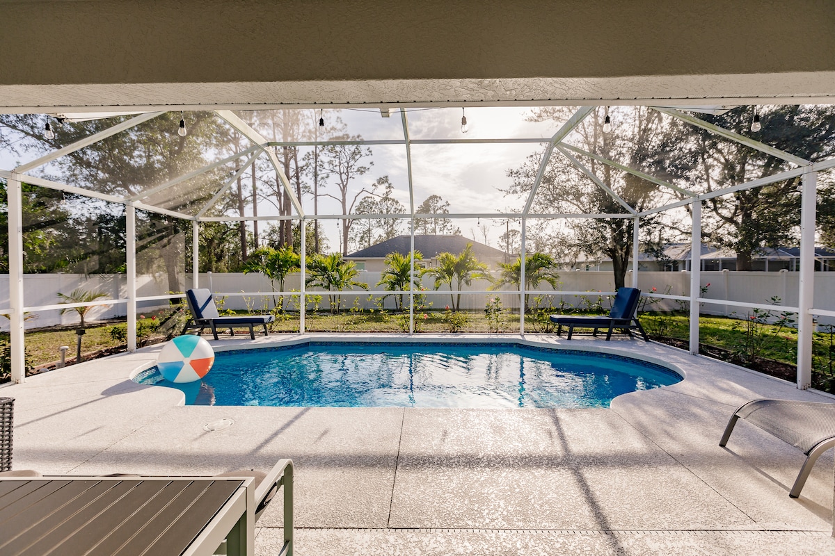 A screened-in lanai surrounds a heated pool, inviting leisure and relaxation. Two lounge chairs sit along one side, with lush greenery and landscaping visible in the background. Natural light bathes the area, enhancing the serene atmosphere. A colorful pool float adds a playful touch.