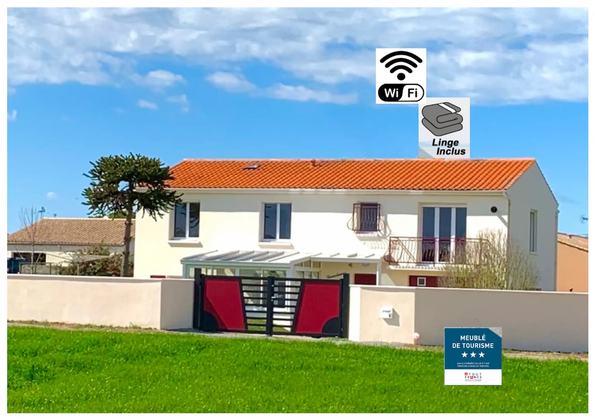 The exterior of the property is shown, featuring a two-story building with a red-tiled roof and white walls. A well-maintained garden area surrounds the entrance, which includes a private gate. Clear blue skies and a green lawn add to the welcoming atmosphere.