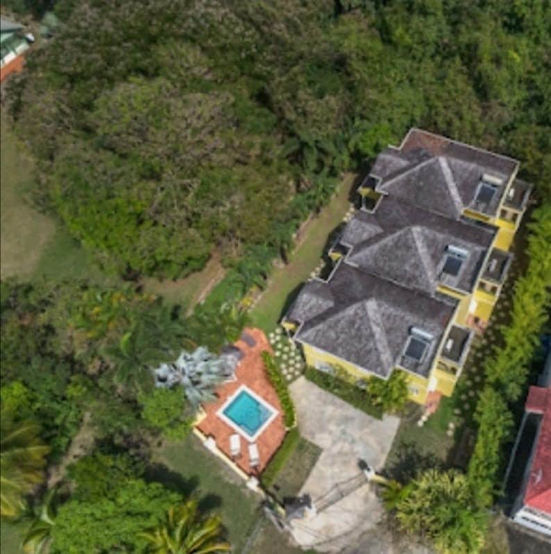 An aerial view captures a luxury villa with three townhouses bordered by lush greenery. A shared pool is visible in the backyard, surrounded by a tiled deck and neatly arranged garden areas. The property is set within a tranquil environment, ensuring privacy.