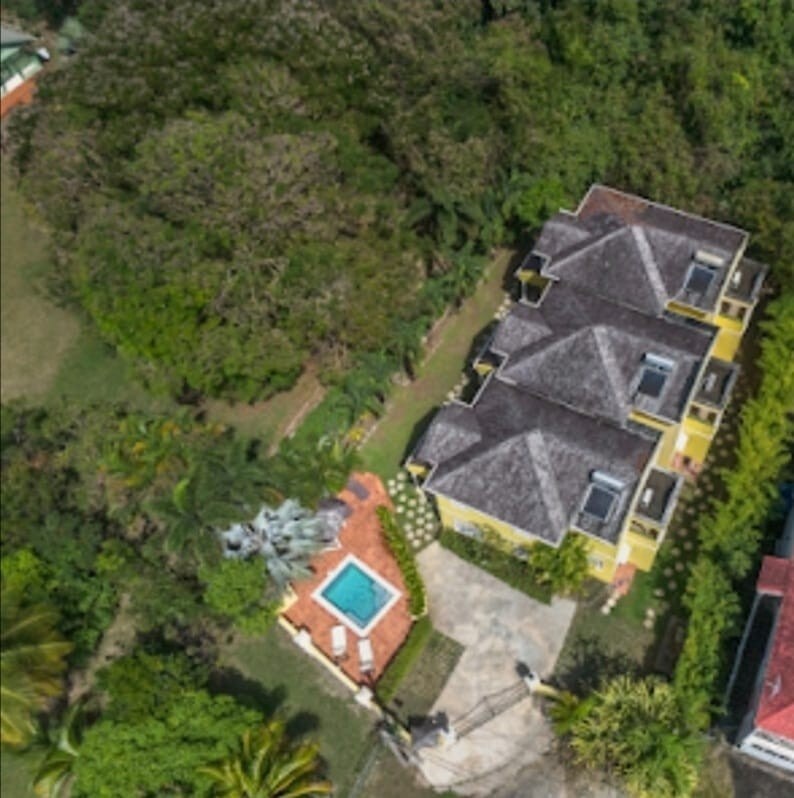 An aerial view showcases a cluster of stylish townhouses, surrounded by lush greenery. A private pool is visible in the center, complemented by landscaped gardens and pathways, creating an inviting outdoor space for relaxation.