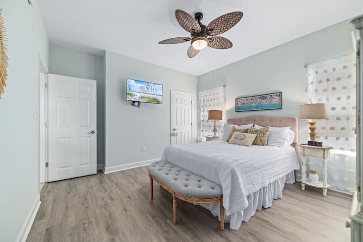 Tufted 2nd king bed with shell pillows, pastel walls, driftwood fan, and coastal artwork.