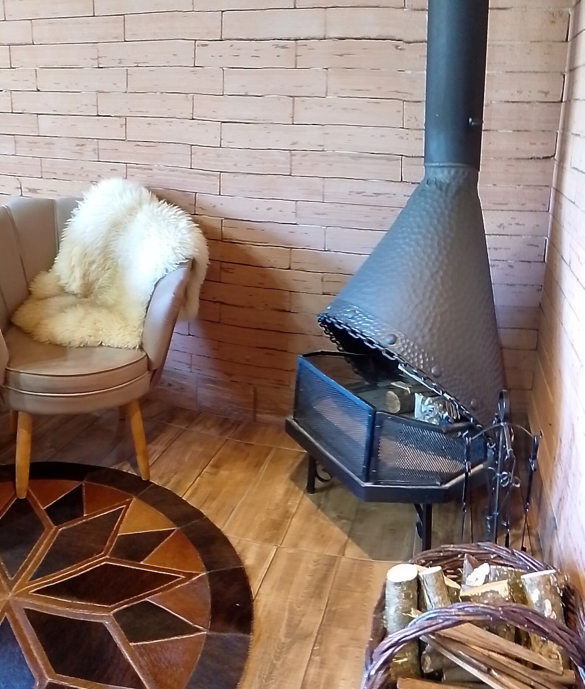 A cozy seating area features a circular area rug with an intricate pattern. A modern fireplace stands in the corner, complemented by a nearby chair draped with a soft, textured throw. A basket filled with logs is positioned beside the fireplace.