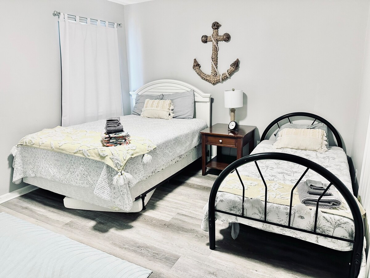 Manželská posteľ Queen vľavo. Dve samostatné postele vpravo. Komoda a nočný stolík v izbe.