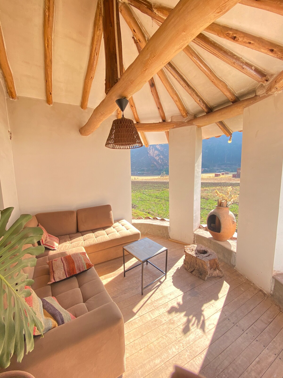 A cozy sitting area is featured with a comfortable sofa and a wooden coffee table. A charming clay fireplace adds warmth to the space, while large windows provide views of the surrounding nature.