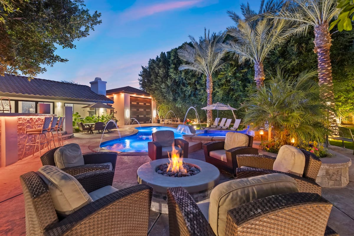 Resort pool and deck lit at dusk with fire pit and palms
