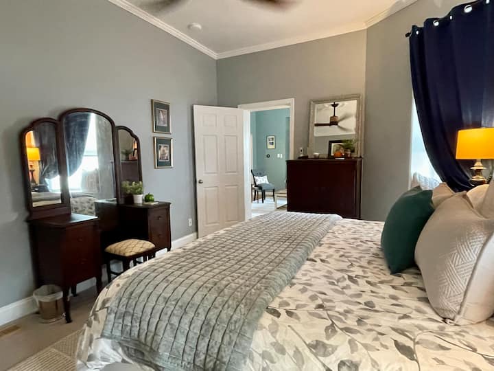 King bedroom that has 4 plush pillows, mirror, blackout curtains, fan, closet space, and a makeup vanity. Luxurious linens, bedding, comfy beds, & blankets.