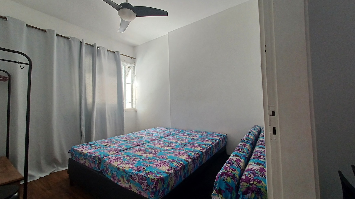 Dos camas individuales con 2 auxiliares y 2 colchones más, almohadas, cortinas negras, ventilador de techo y Arara con perchas. Vista lateral del mar.