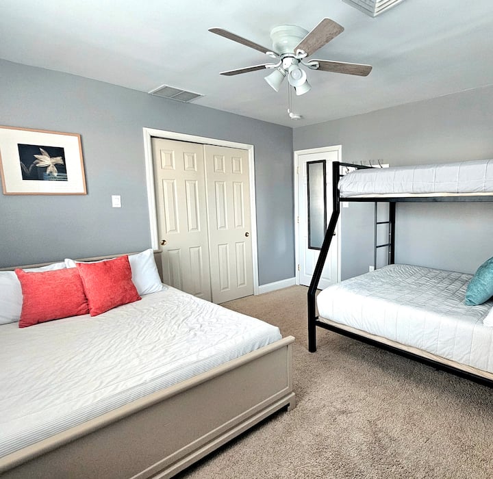 Оваа спална соба има голем брачен кревет и кревет на спрат со кревет за едно лице над брачниот кревет. 