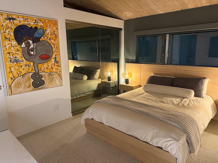 Queen bed with modern floating nightstands and 65" Sony 4K TV — true blackout shades.