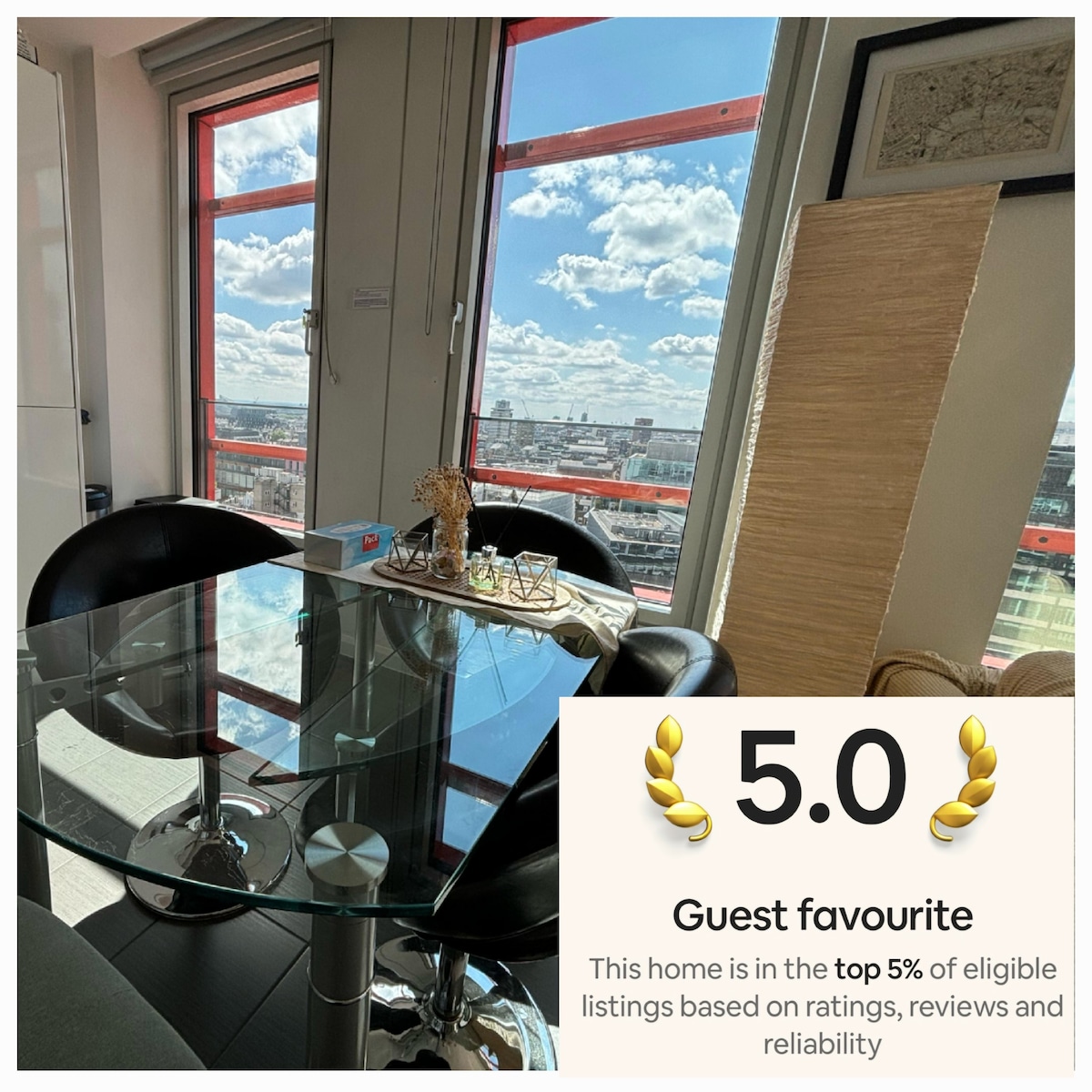 A glass dining table is positioned beside large windows, allowing natural light to fill the space. The table is complemented by black chairs and a decorative vase. Views over London are visible in the background, with varied cloud patterns enhancing the outdoor scene.