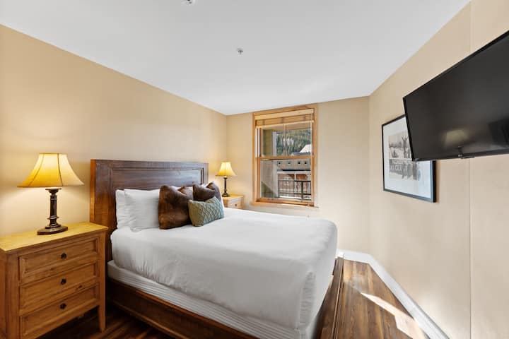 בחדר השינה לאורחים יש מיטת קווין סייז עם מצעים בצבע לבן שנהב וטלוויזיה עם מסך שטוח.