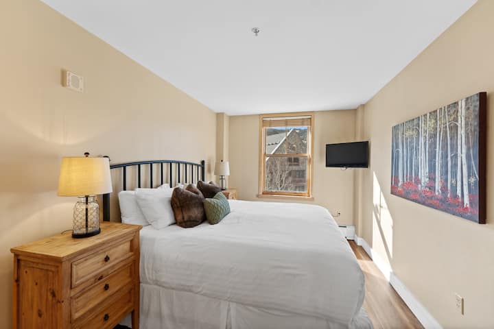 חדר השינה הראשי כולל מיטת קינג סייז עם מצעים בצבע לבן שנהב, טלוויזיה עם מסך שטוח וחדר רחצה צמוד. 