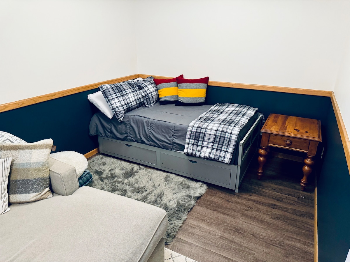 E vendosur brenda zonës së ndenjjes së nivelit më të ulët, kjo zonë e dhomës së gjumit është e përkryer për fjetje shtesë ose kohë të qetë. Krevati dopio me trungje tërhiqet për të bërë një mbret me shtroja krevati të vendosura poshtë. Komodina plotëson hapësirën.