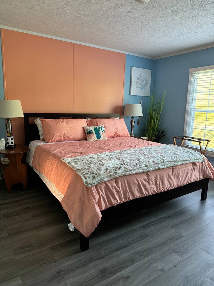 Kingsize-Bett im Hauptschlafzimmer. Während der verschiedenen Jahreszeiten kann es sein, dass das Zimmer, die Einrichtung und/oder die Bettwäsche verändert wurden. Es gibt einen kleinen grauen Sessel, der in ein Einzelbett umfunktioniert werden kann. Die Bettwäsche liegt im Hauptbadezimmer auf dem unteren Regal.