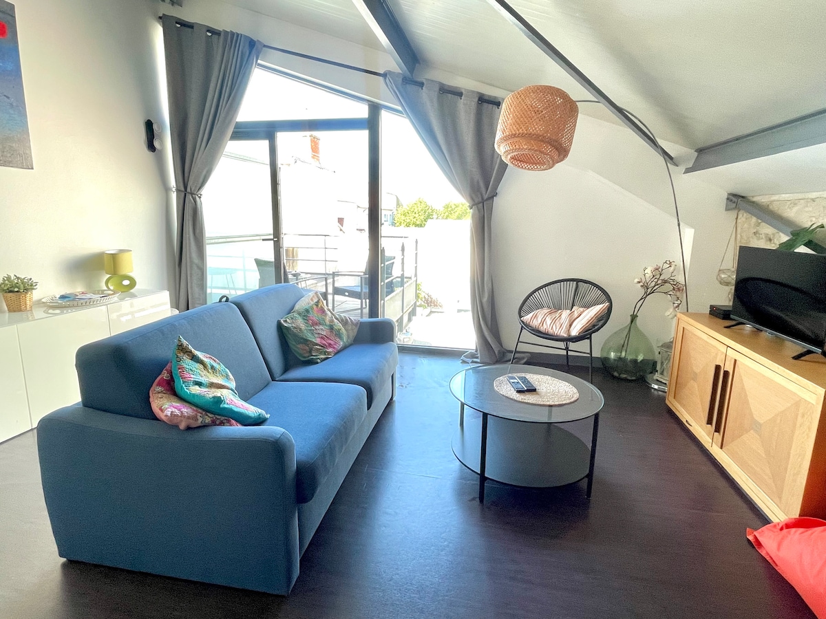 A well-lit living area features a blue sofa adorned with decorative cushions, complemented by a round coffee table. Large glass doors open to a balcony, allowing natural light to fill the space. Drapes frame the windows, enhancing the cozy appeal.