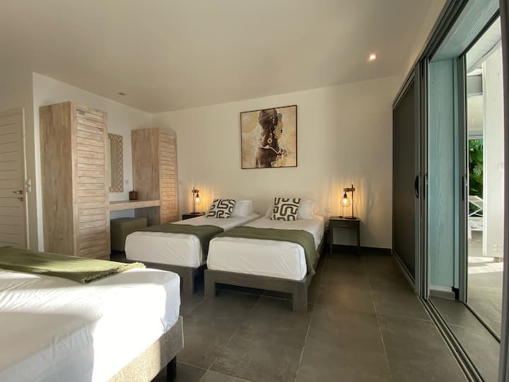 Spavaća soba s 3 kreveta za jednu osobu ili soba s jednim bračnim krevetom i jednim krevetom za jednu osobu. Ima izlaz na terasu i plažu Grande Anse i privatnu kupaonicu. Vila Coco Cannelle Prestige s 5 zvjezdica