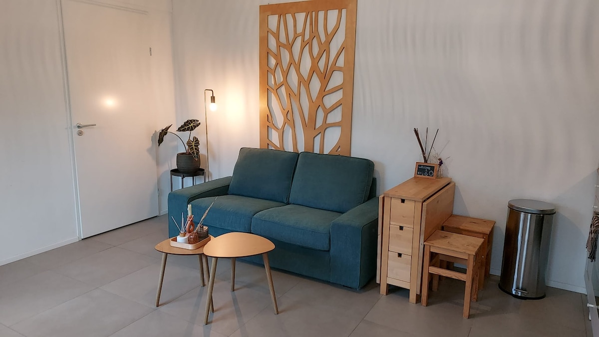 A living area showcases a turquoise sofa, supported by wooden side tables for functionality. A decorative wall panel with an abstract tree design adds interest. Soft lighting is provided by a standing lamp, complemented by a small plant arrangement nearby.
