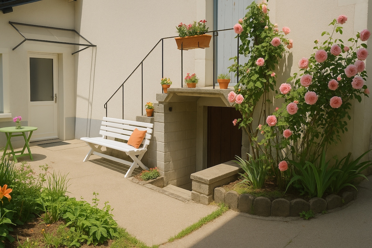 A welcoming outdoor space features a white bench positioned beside a small green table. Vibrant pink roses climb the adjacent wall, while flower pots add color to the area. A staircase leading to the entrance is accompanied by a charming stone fireplace.