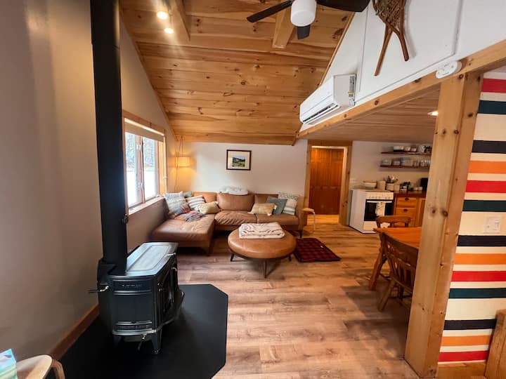 Looking east, Vermont castings wood burning stove, sectional leather sofa and ottoman, open living room/dining/kitchen/entryway area