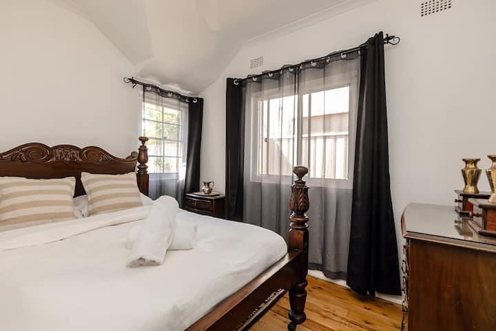 Bedroom 2 offers a peaceful, relaxed atmosphere for guests, featuring a historic solid timber queen bed and original period details. The space is highlighted by polished timber floors and abundant soft natural light.