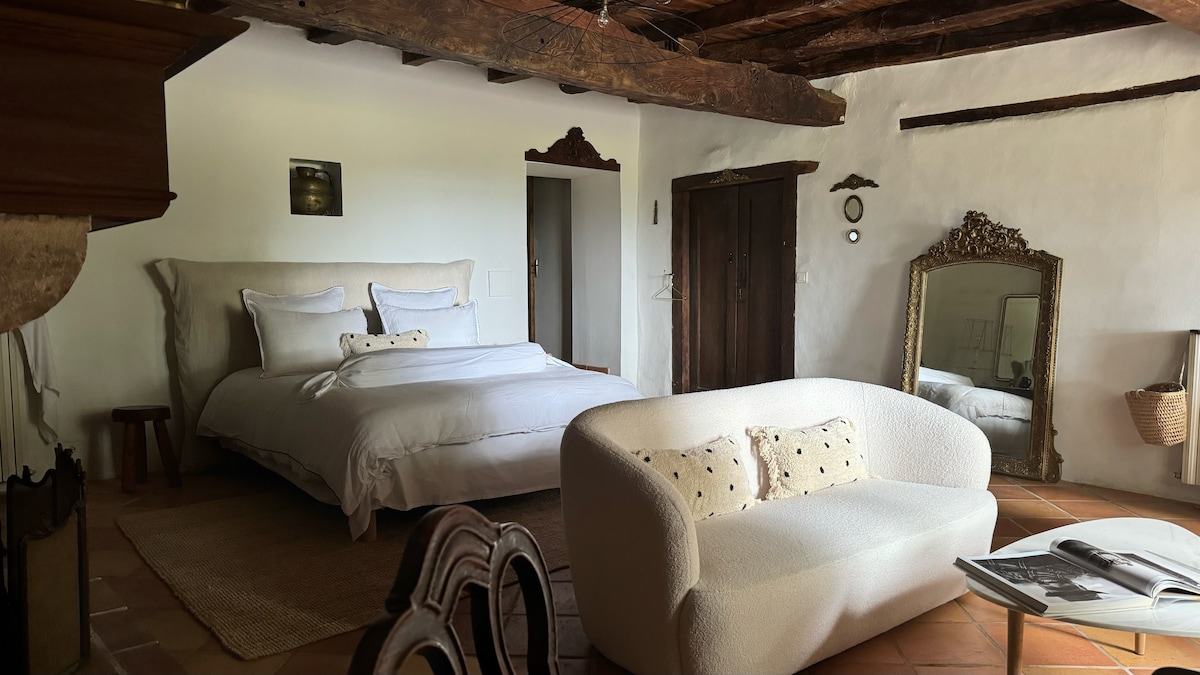 En esta habitación hay una cama, un sofá, una mesa de centro, una cómoda y una mesa con 2 sillas. 