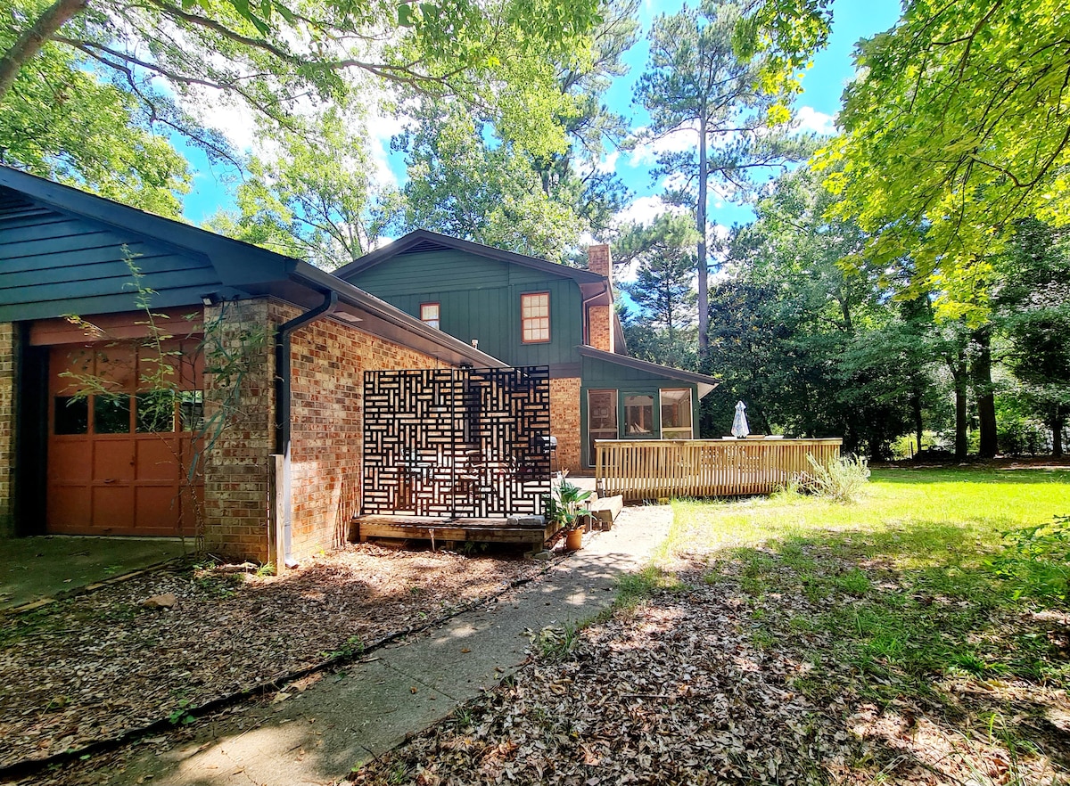 The exterior of the spacious home features a blend of brick and wood siding, with a two-car garage visible on the left. A wooden deck is situated at the back, surrounded by greenery, offering a serene outdoor space for relaxation.