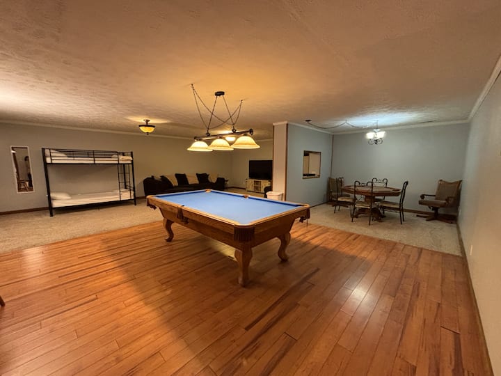 Game room in the basement with a table to play games on, pool table, bunk beds for sleeping, and a 65" tv.