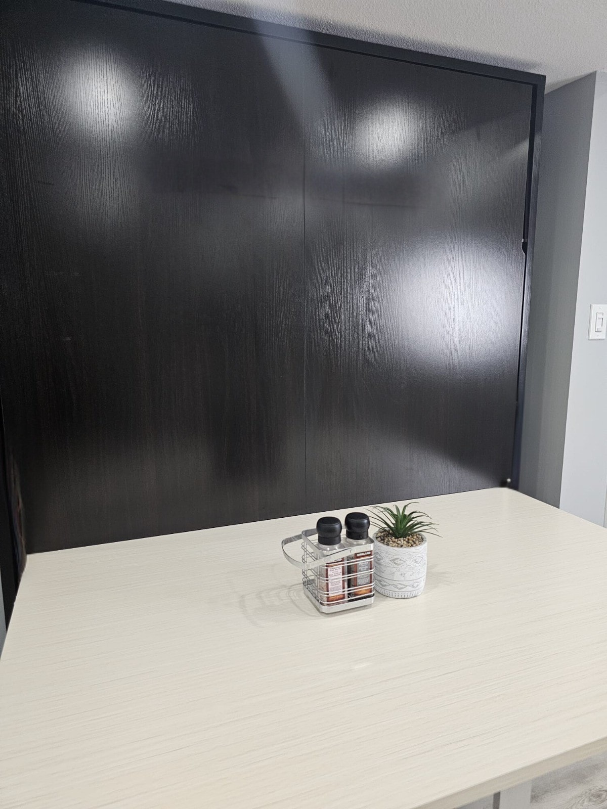 A functional workspace is displayed with a light-coloured tabletop, accompanied by a small potted plant. In the background, a dark wooden cabinet is visible, creating a contrast with the lighter surfaces in the space.