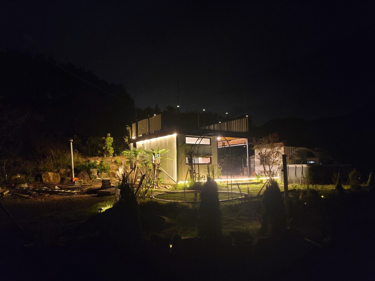 The structure is illuminated at night, with soft lighting outlining its contours. Surrounding greenery and a garden area are visible, creating a serene atmosphere. The night sky serves as a backdrop, enhancing the peaceful setting.