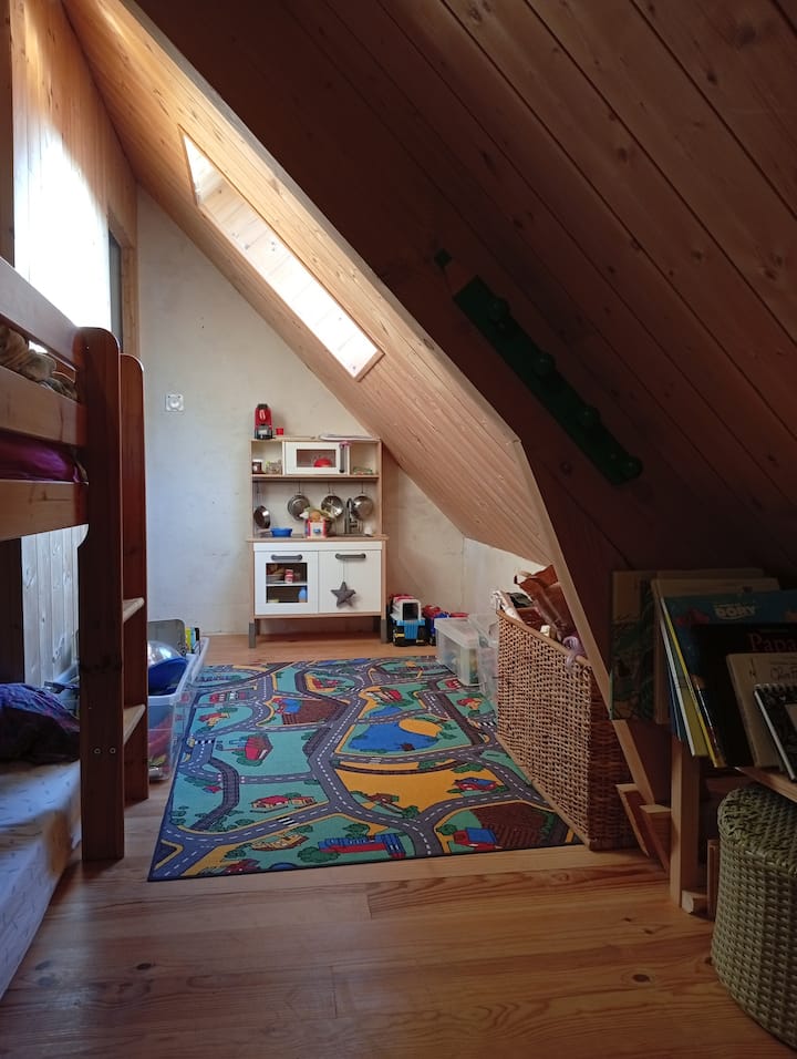 Тази малка детска спалня под тавана има две единични легла, едно от които е високо. На разположение са някои играчки и детски книжки.