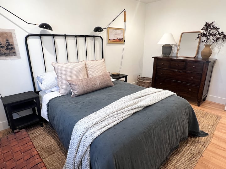 Comfortable queen bed with sconces, leather bench and wood dresser.