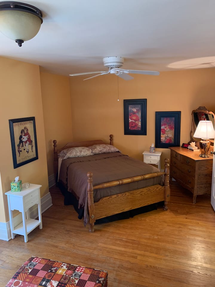 El dormitorio completo tiene tres espacios en uno: área para dormir con cómoda, sofá de dos plazas con televisión inteligente y chimenea eléctrica, y sección de oficina con espacio de presentación para reuniones en línea. 