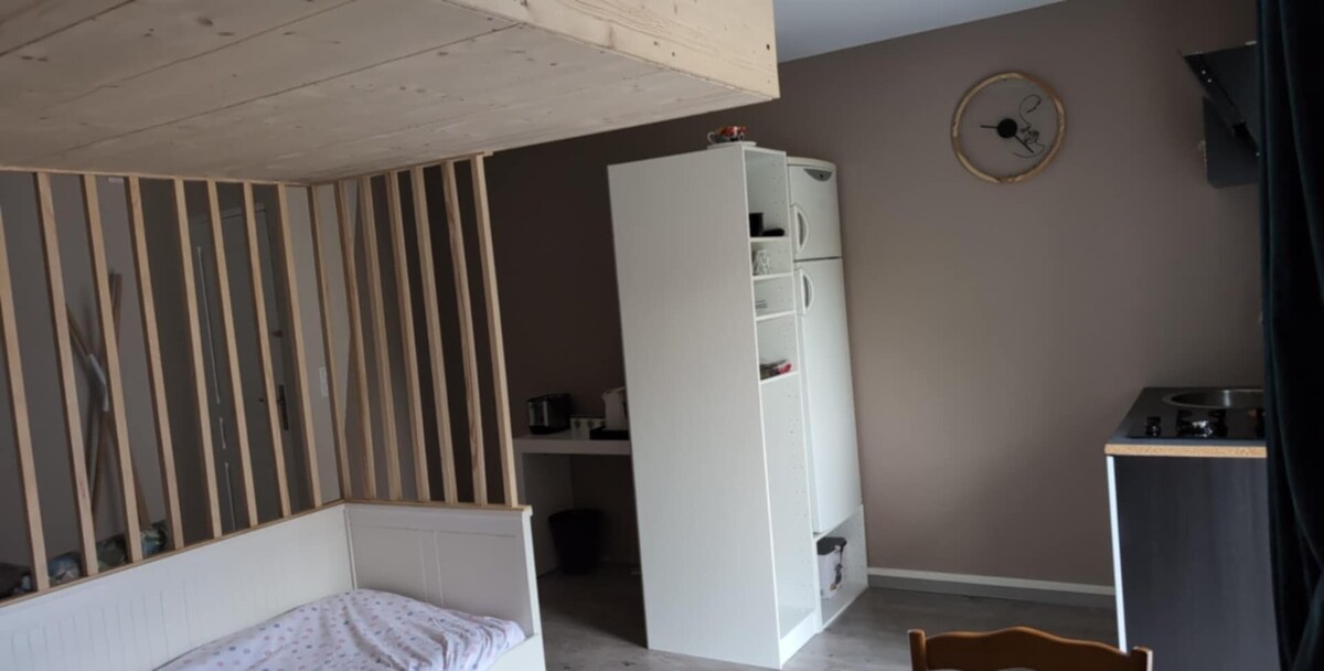 A bright and minimalist studio showcases a designated sleeping area with a cozy bed. A spacious kitchen is equipped with essential appliances, complemented by a modern cabinet. Light walls enhance the sense of openness, while neutral tones contribute to a calm environment.