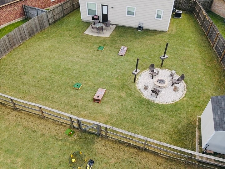 A spacious backyard is enclosed by a wooden fence, featuring a fire pit surrounded by seating. Lawn games are set up on the grass, with a picnic table nearby. A well-maintained lawn provides ample space for outdoor activities.
