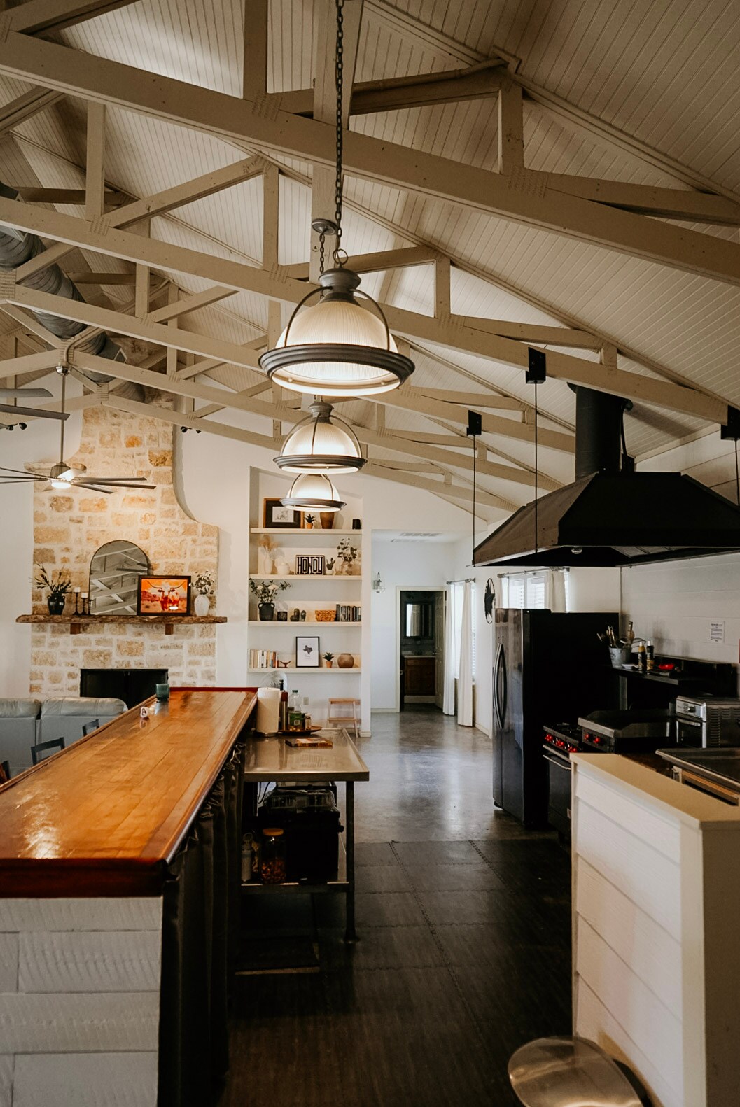 The spacious kitchen is highlighted by vaulted ceilings and warm wood accents. A large island provides additional seating and storage. A rustic stone fireplace is visible in the background, accompanied by modern appliances, including a commercial-grade stove.