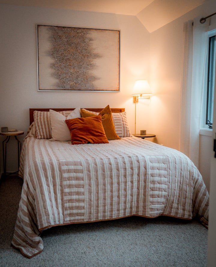 Second story full bedroom with views of the back deck and forested ravine. Large textural art centered over the headboard with a new memory foam mattress. Cozy and calm, with plenty of space to rest after a day exploring.